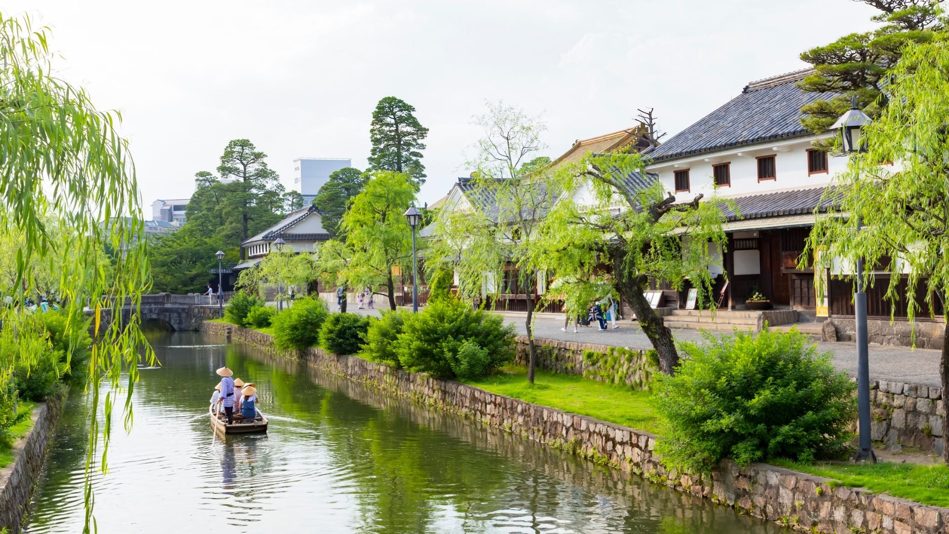 Turisti su una barca tradizionale lungo il canale del quartiere storico di Kurashiki Bikan, circondato da salici e case d'epoca del periodo Edo, parte dell'itinerario "Giappone classico ma...