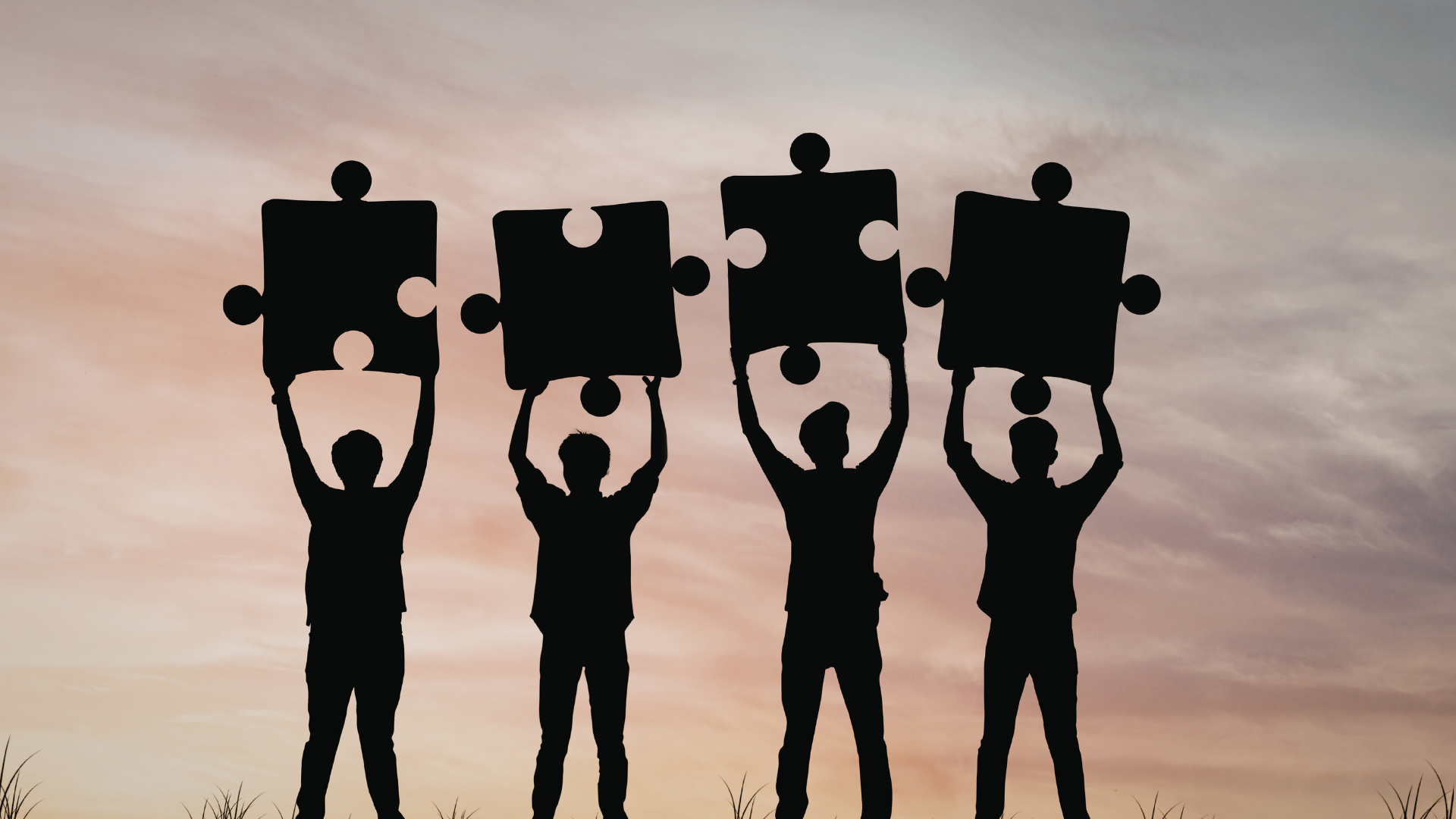 Silhouette di quattro persone che sollevano grandi pezzi di un puzzle coordinati verso un cielo al tramonto; l'immagine rappresenta metaforicamente la partnership strategica e il completamento del progetto di internazionalizzazione in Giappone offerto da Hidden Japan Business.